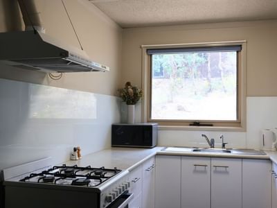 Modern kitchen with white appliances, microwave, sink, and window view at La Trobe University Villas.