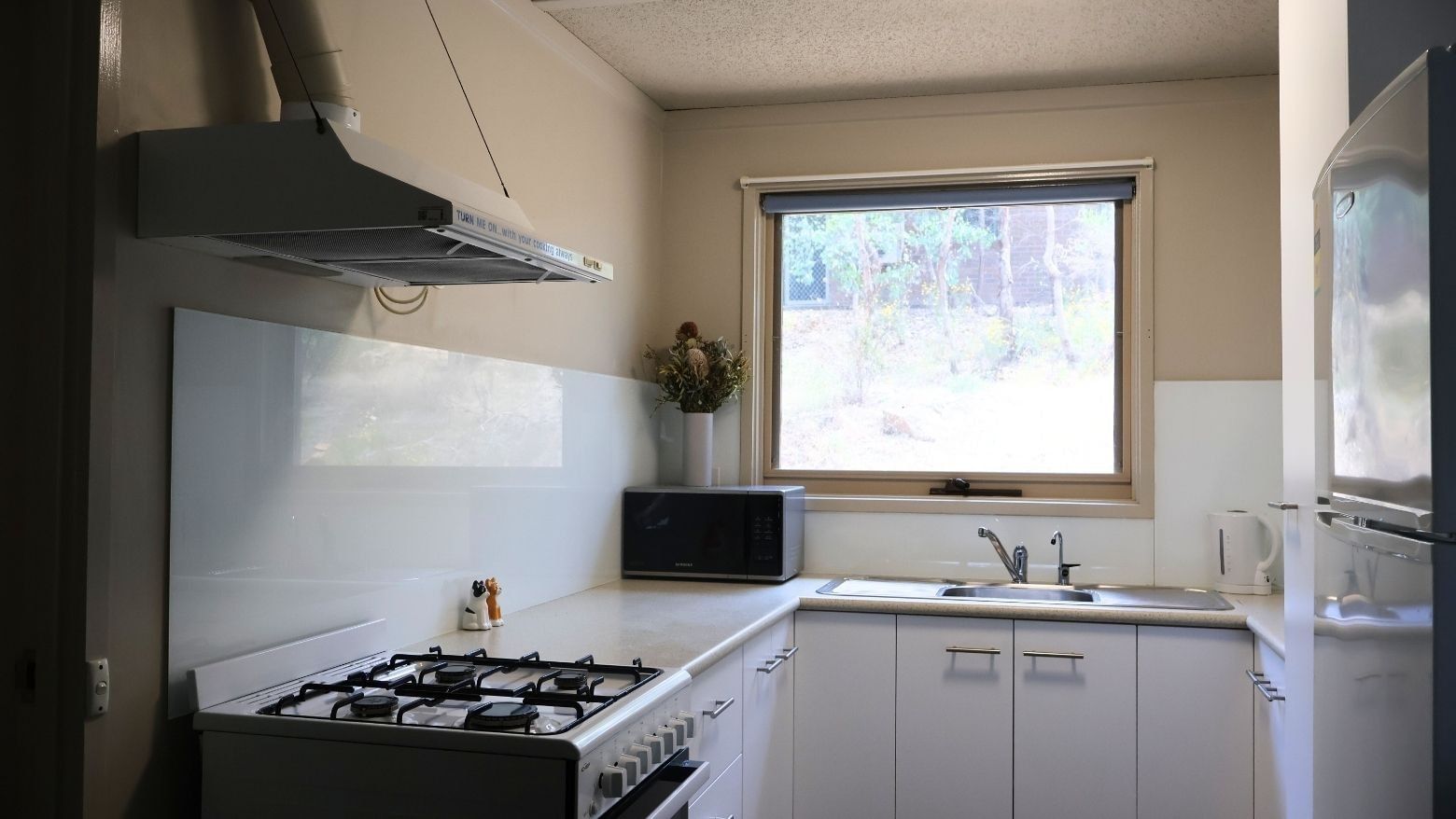 Modern kitchen with white appliances, microwave, sink, and window view at La Trobe University Villas.