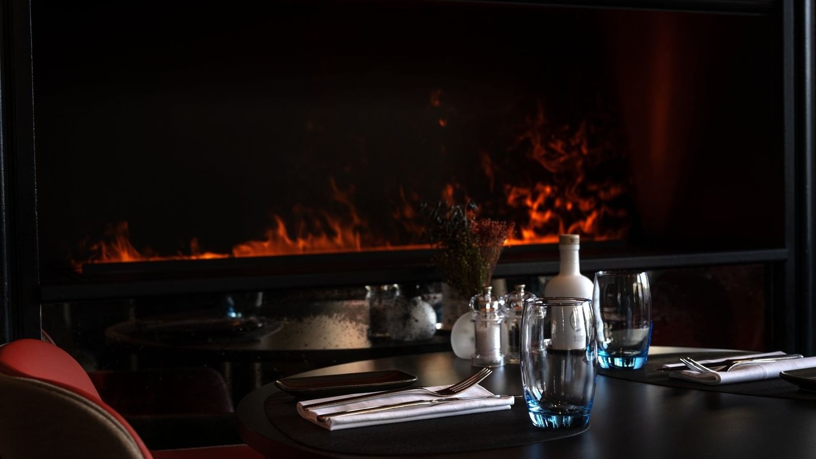Glassware on a dark table by a glowing fireplace under soft, moody light in Téséo at Warwick Geneva
