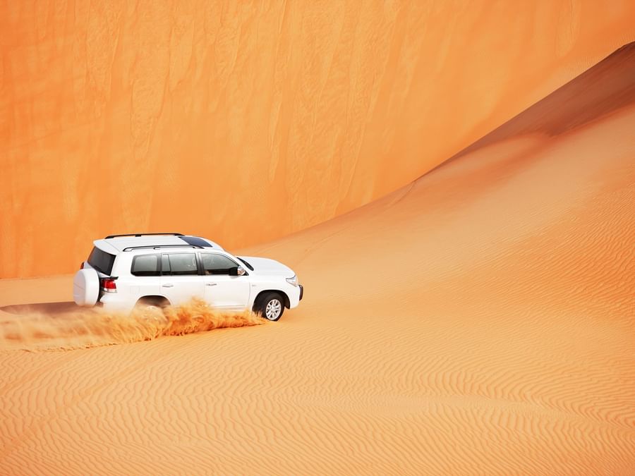 White jeep driving through desert dunes near DAMAC Hotels & Resorts, the best luxury hotel in Dubai