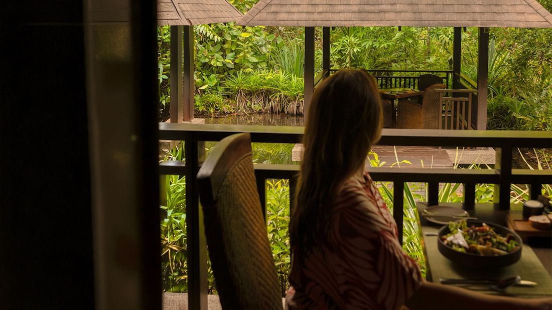 Woman dining on a balcony with lush garden and hot spring view in The Banjaran offer.