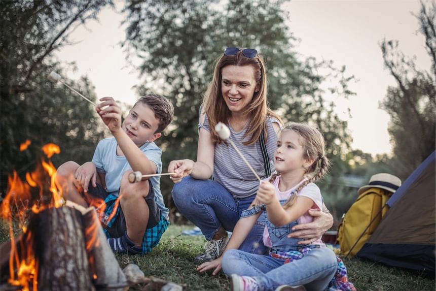 Mother and two children are sitting around a campfire, roasting marshmallows at Fall Creek Marina & Campground