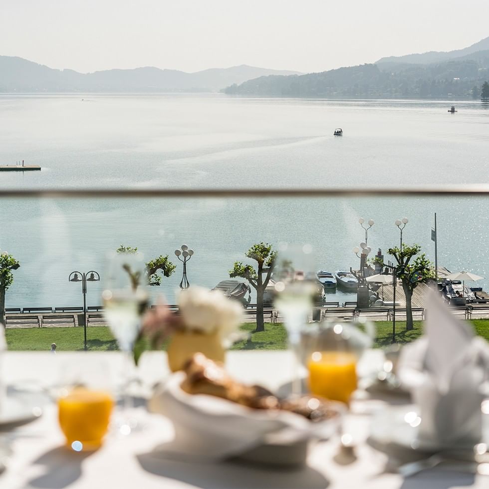 Breakfast table with wine and orange juice overlooking a calm lake and distant mountains.