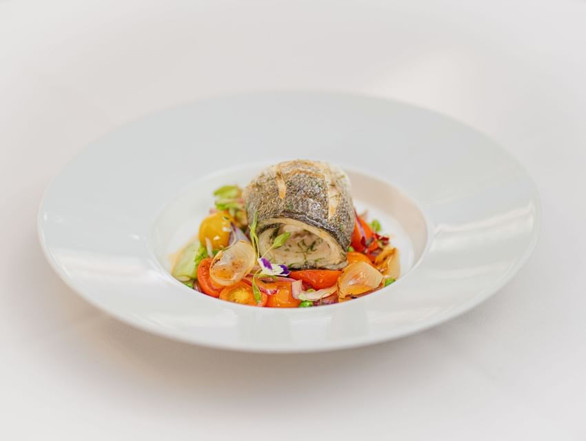 Rolled fish fillet served with roasted vegetables and cherry tomatoes on a plate in Tudors Restaurant at Marygreen Manor