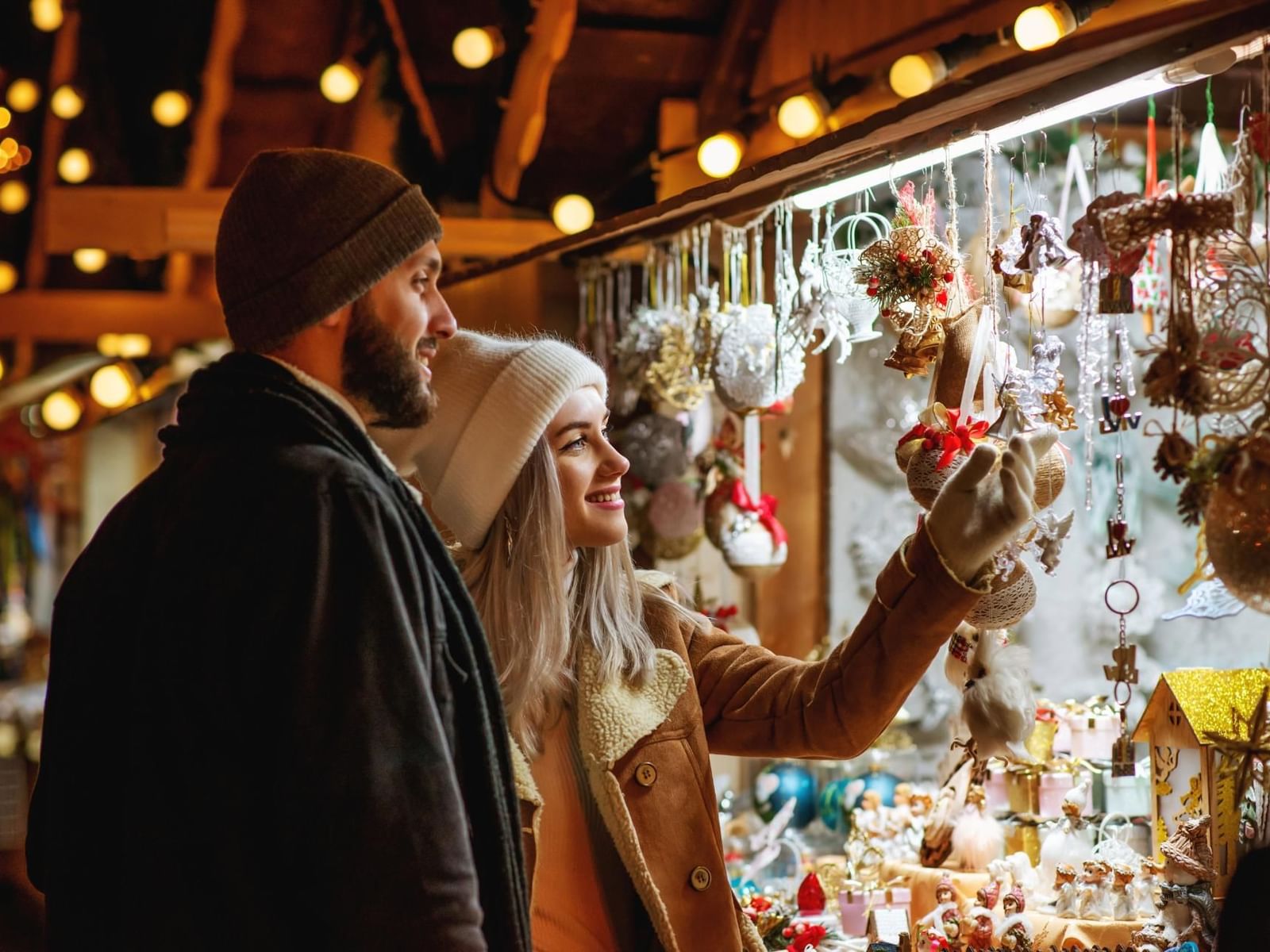 A couple admires festive ornaments at the Piazza Navona Christmas Markets, surrounded by warm lights near The Guardian Hotel