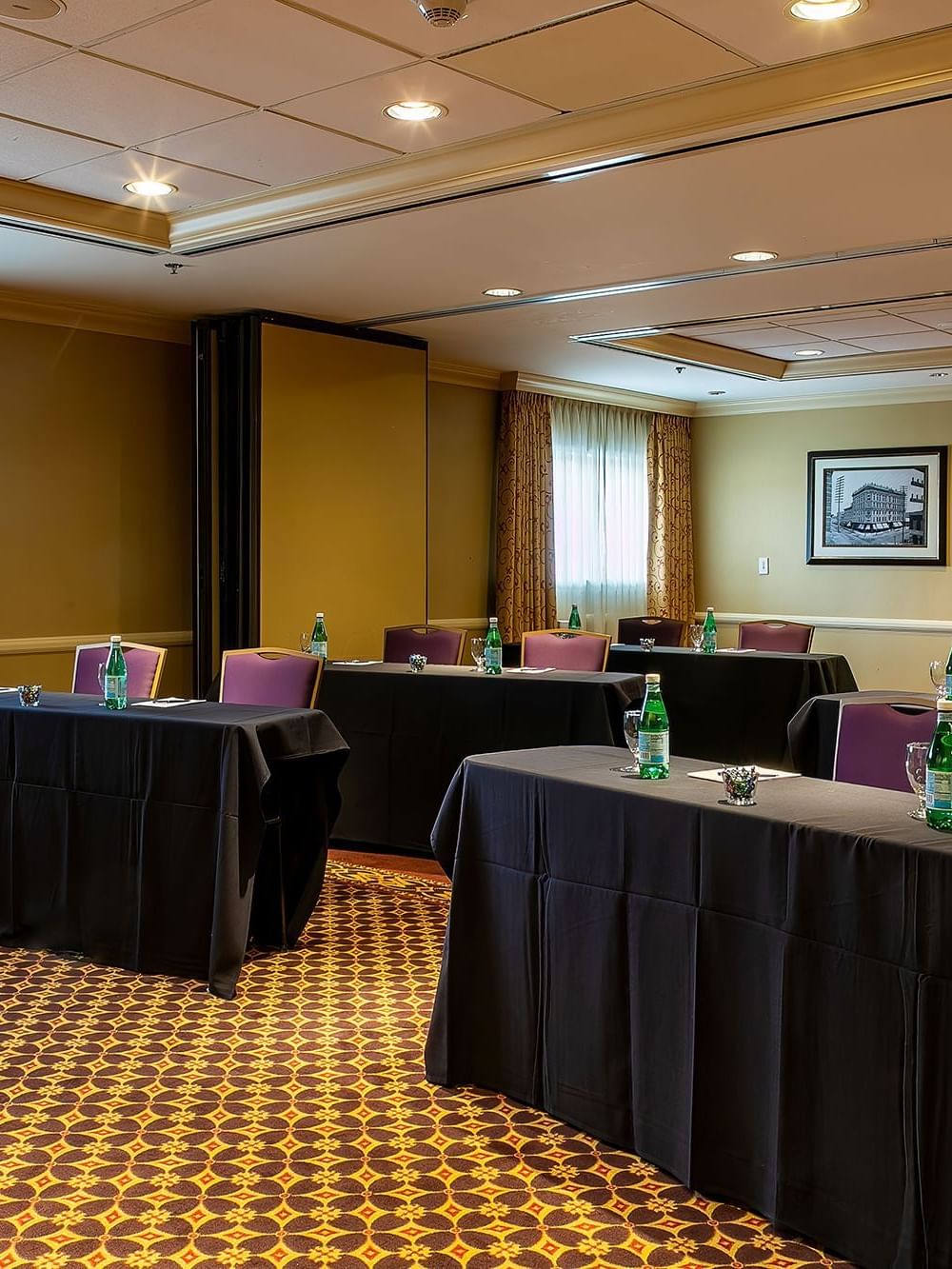 Black clothed tables by purple chairs under recessed lights in Tabor at Warwick Denver