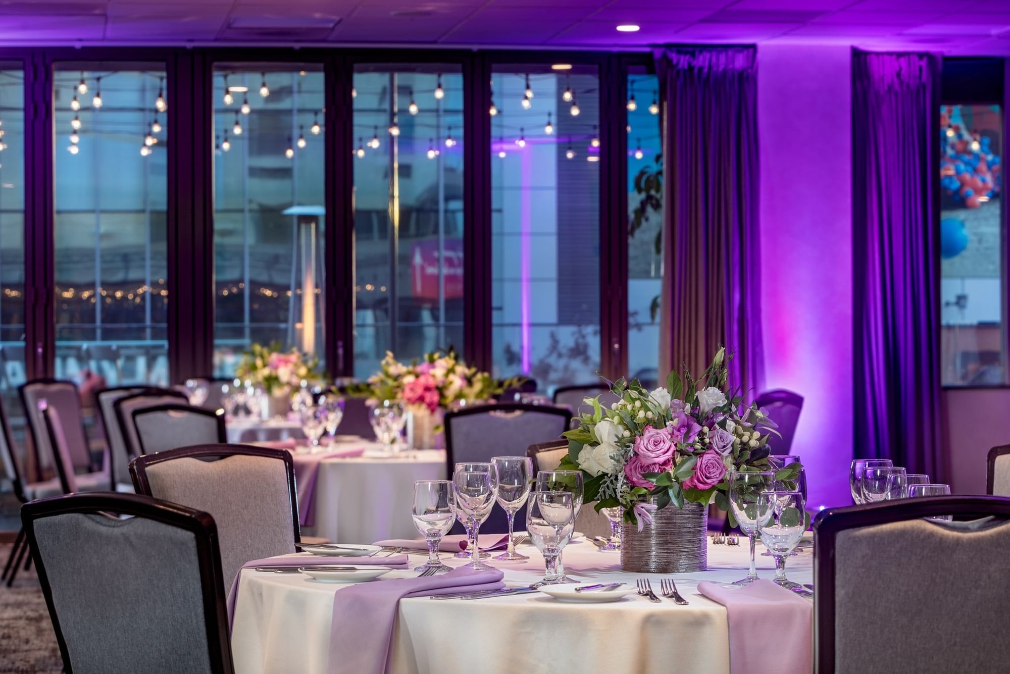 A dining room with round tables set with white tablecloths, flowers, and glassware.