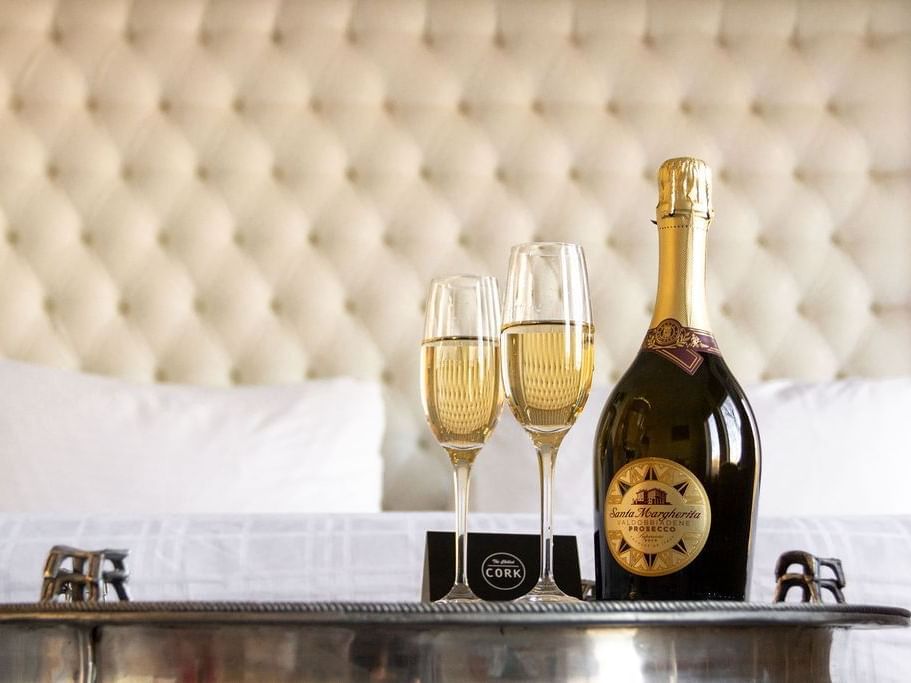 A bottle of Prosecco & 2 glasses by a bed at Retro Suites Hotel