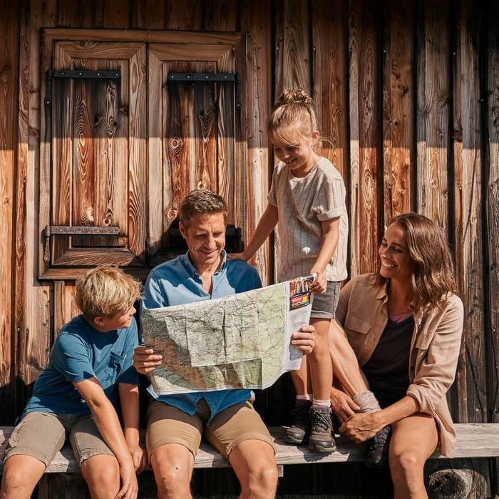 Famiglia seduta su una panchina di legno, guardando una mappa con un sorriso.