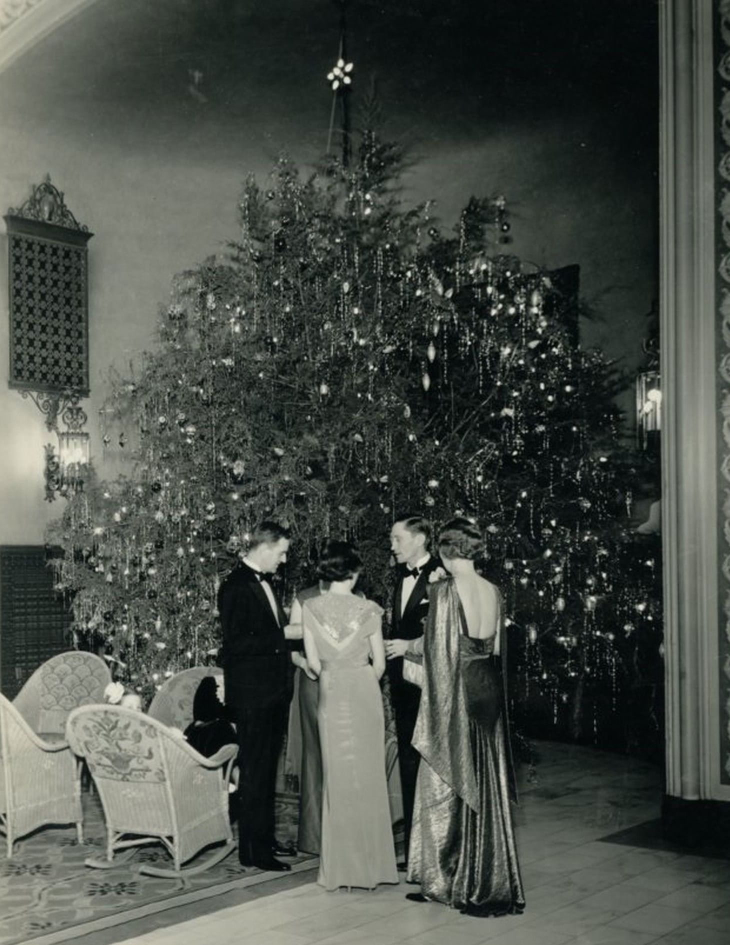 Vintage image of formal guests by wicker chairs under a tall decorated Christmas tree at Arlington Resort Hotel & Spa