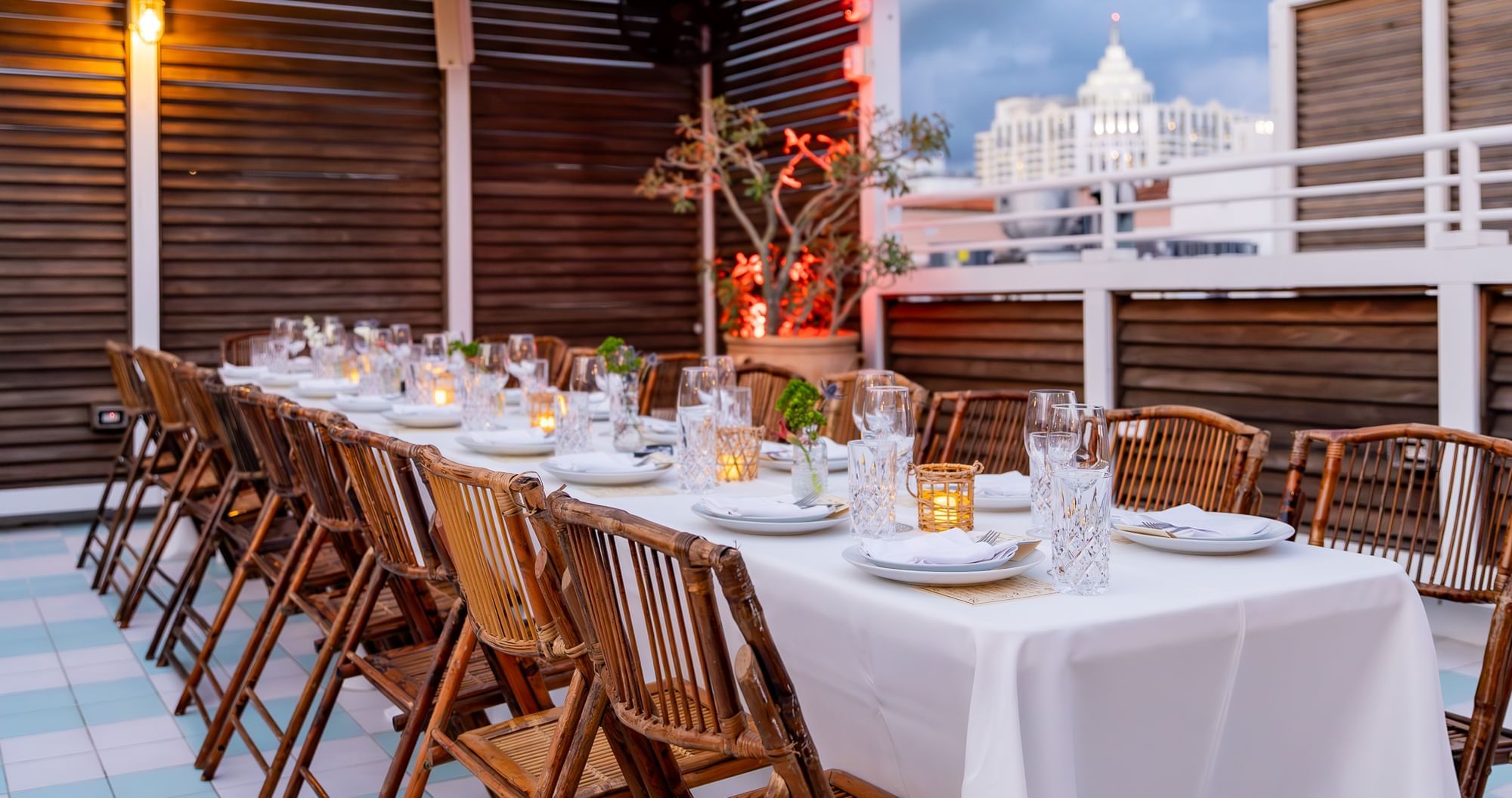 A long table set for dinner on an outdoor patio with a city view.