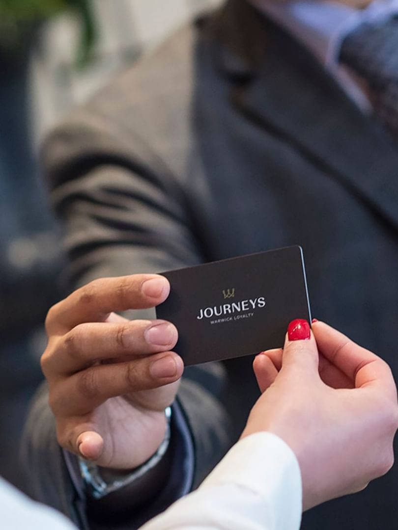 Guest holding a loyalty card by a staff member under soft light at Warwick Melrose Dallas