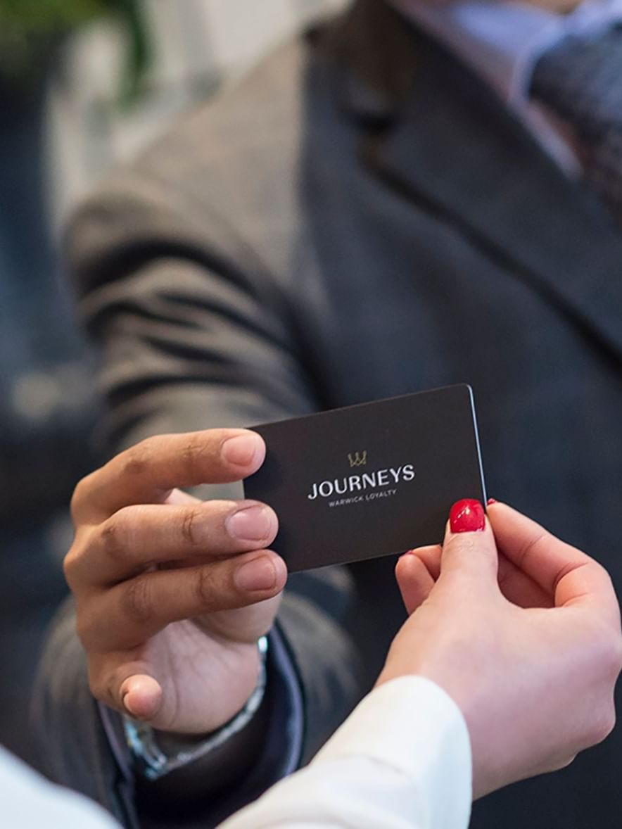 Guest holding a loyalty card by a staff member under soft light at Warwick Melrose Dallas