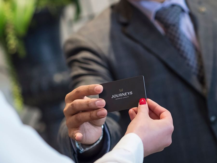 Guest holding a loyalty card by a staff member under soft light at Warwick Melrose Dallas