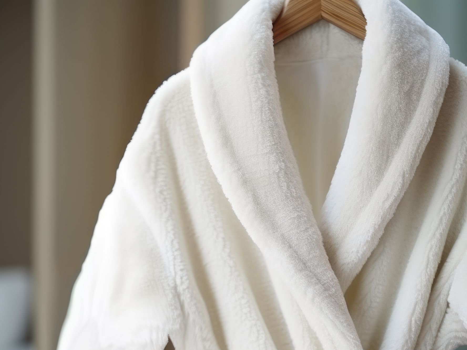 A plush, white hotel bathrobe hanging on a wooden hanger in a bright room, representing the comfort of an extended stay at Hotel Grand Chancellor Townsville.