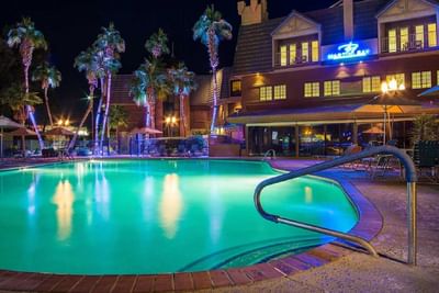 Illuminated outdoor pool with palm trees and multi-story resort building at night at London Bridge Resort