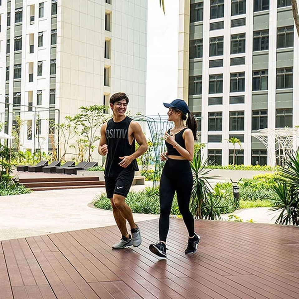 A couple posing with gym outfits on a wooden floor area outdoors at LK Cikarang Hotel & Residences