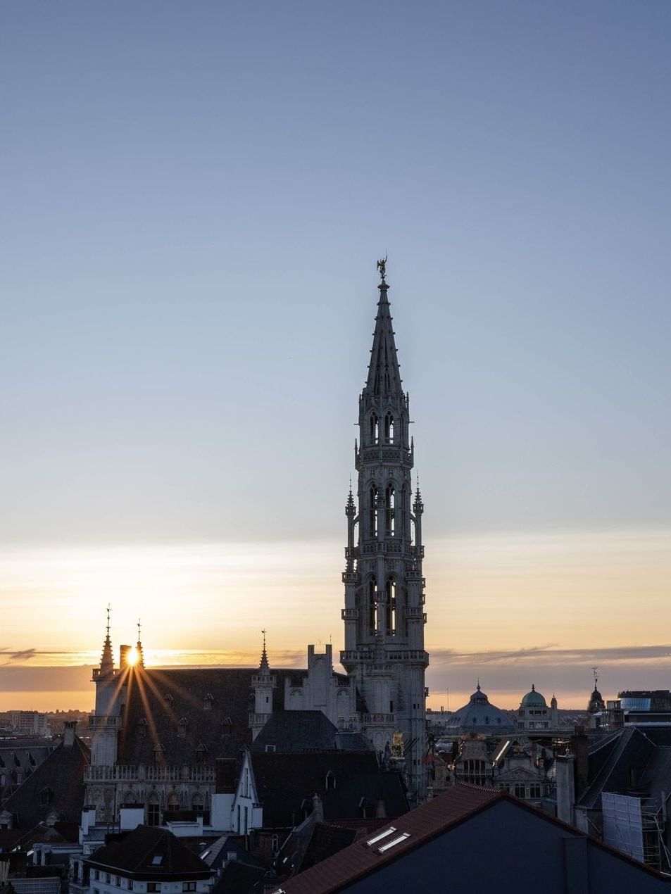 Stunning sunset view of the historic tower placed by city rooftops under a glowing horizon at Warwick Grand Place Brussels