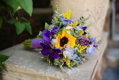 Wedding bouquet with sunflowers, purple and blue flowers, resting on a stone ledge at The Ranch at Ucross