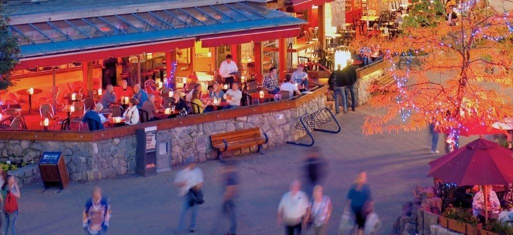 Guests enjoying outdoor dining at a lively Whistler restaurant patio during the evening.