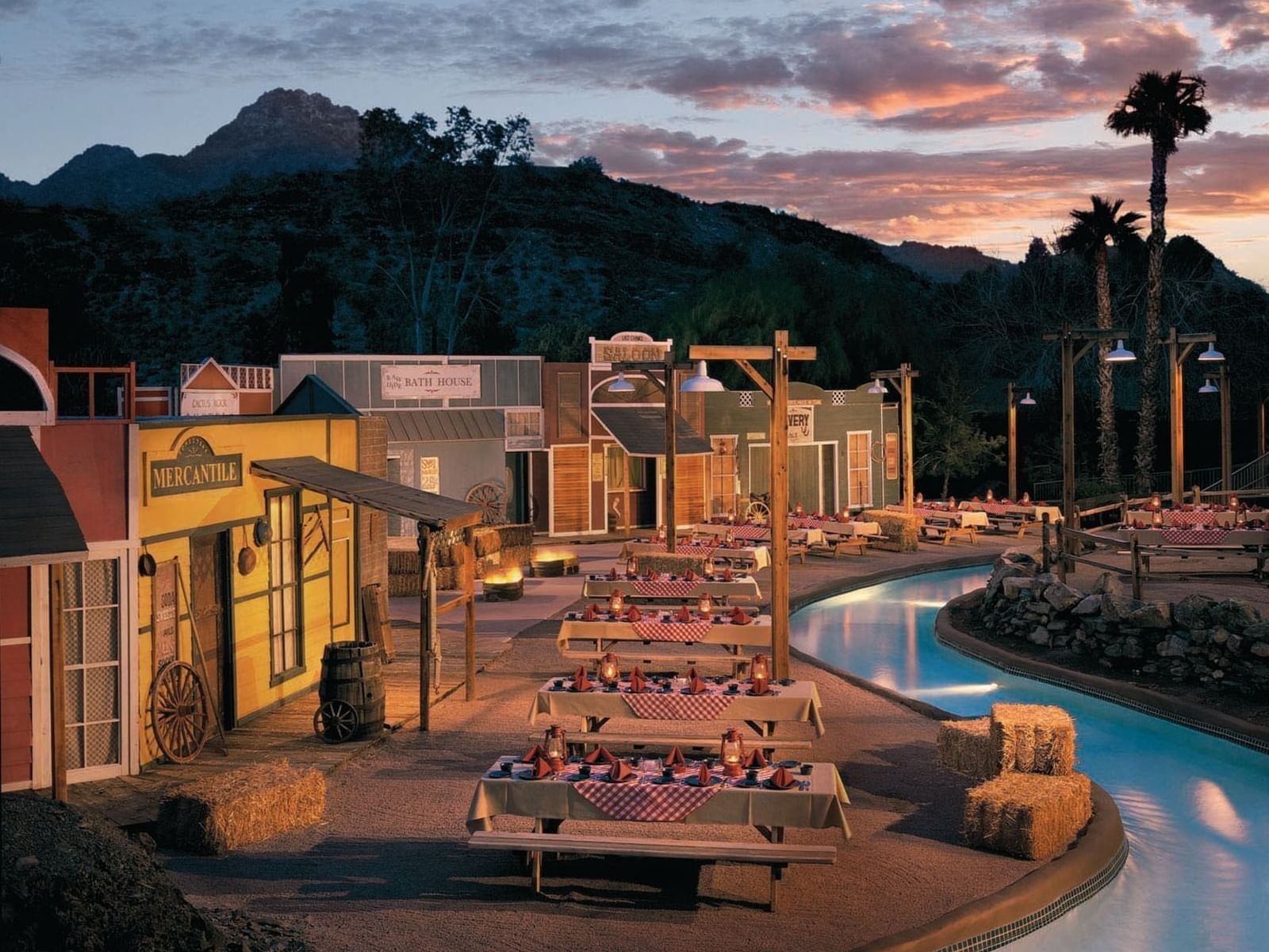 Outdoor Western-themed event space with picnic tables and Old West storefronts at dusk at Hilton Phoenix at the Peak