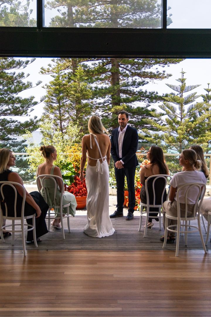 Elysium Manly outdoor wedding ceremony showing a bride facing the groom with seated guests in the background