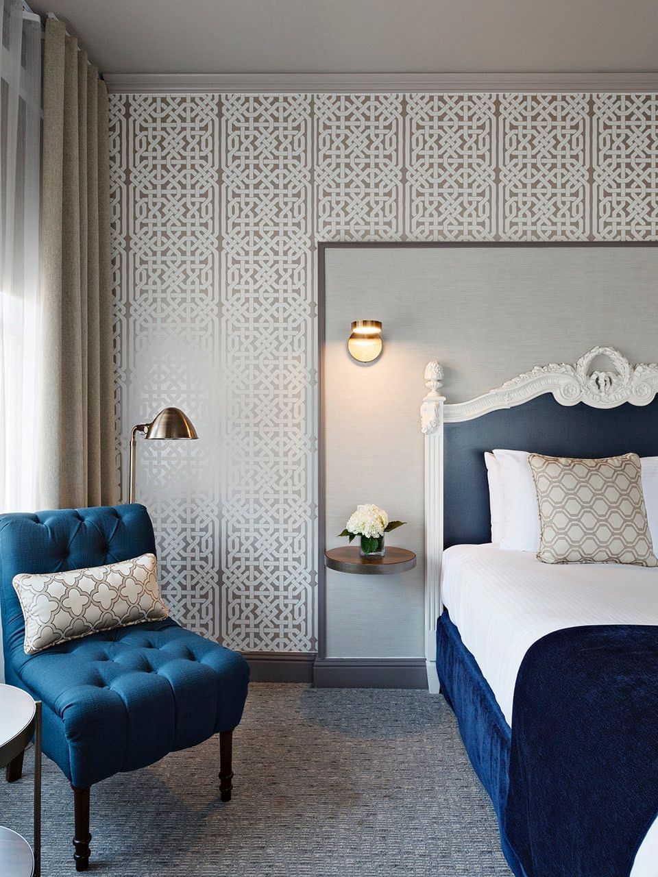 Blue armchair by a tiered table near a bed under an ornate headboard in Corner Deluxe Room at Warwick San Francisco