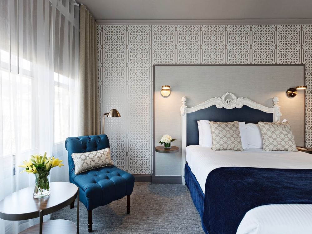 Blue armchair by a tiered table near a bed under an ornate headboard in Corner Deluxe Room at Warwick San Francisco