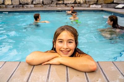 Girl posing by pool wall as water glistens around her, with others playing in the background at Blackstone Mountain Lodge