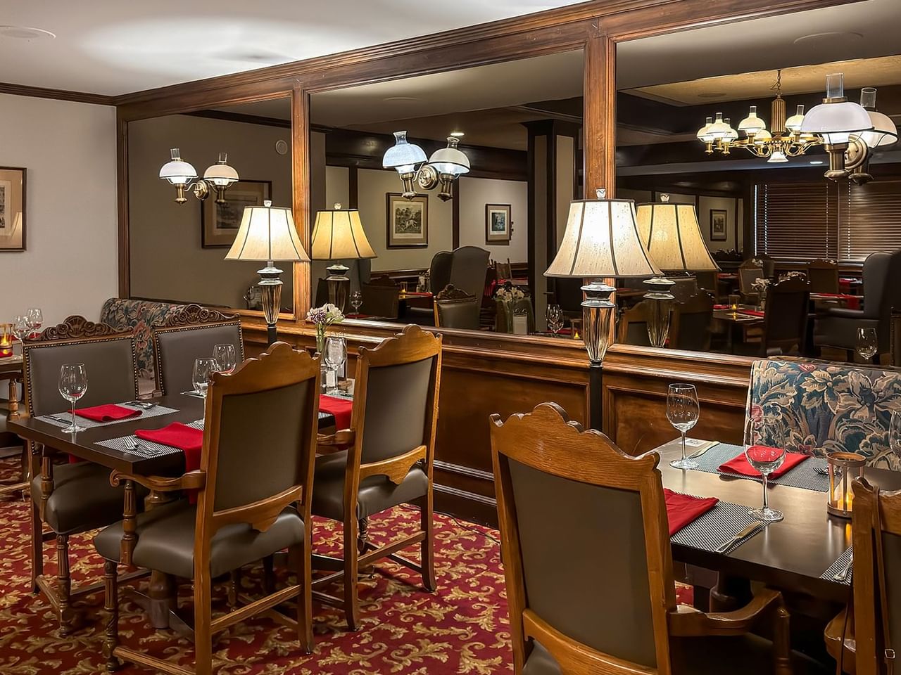 Elegant dining room with wooden tables, cushioned chairs, red tablecloths, and decorative lamps.