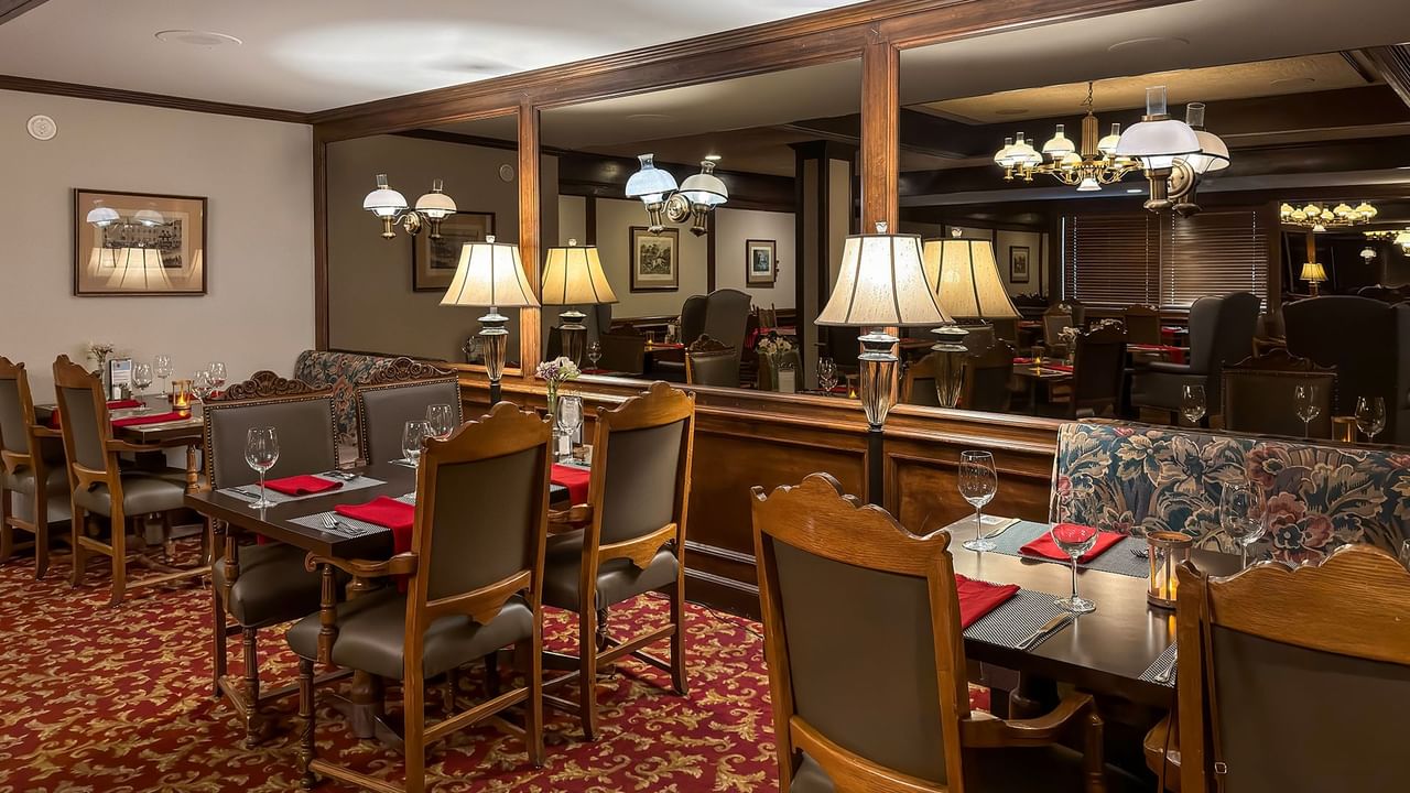 Elegant dining room with wooden tables, cushioned chairs, red tablecloths, and decorative lamps.