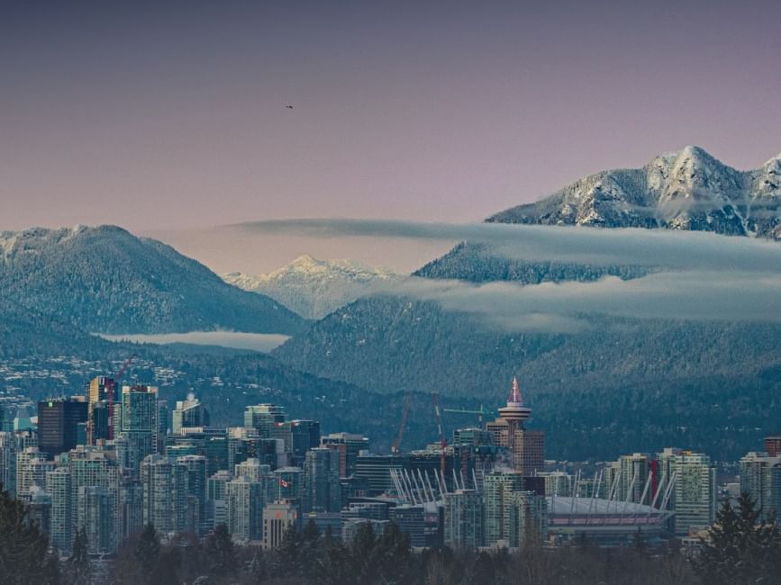 City skyline with modern buildings and snowy mountains in the background.