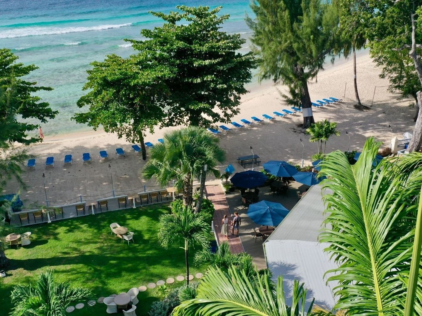 Aerial view of the beach and hotel with green trees and umbrellas.