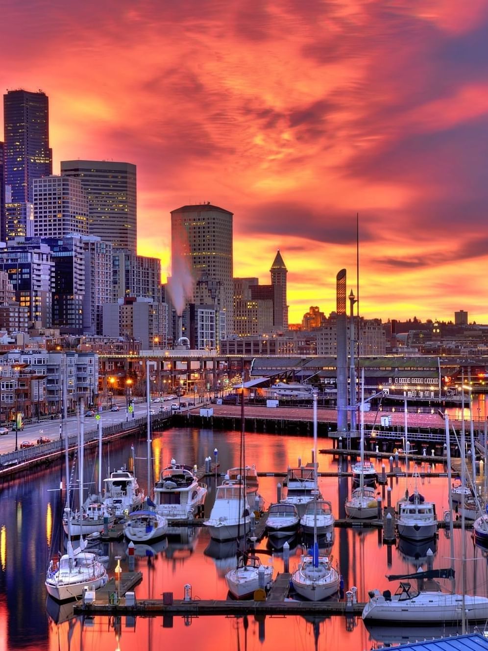 Boats docked in a harbor by city buildings under a vibrant orange sunset near Warwick Seattle