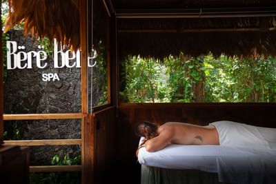 Person lying on a massage bed in Bërë Bërë Spa, surrounded by lush greenery at Le Cameleon Boutique Hotel