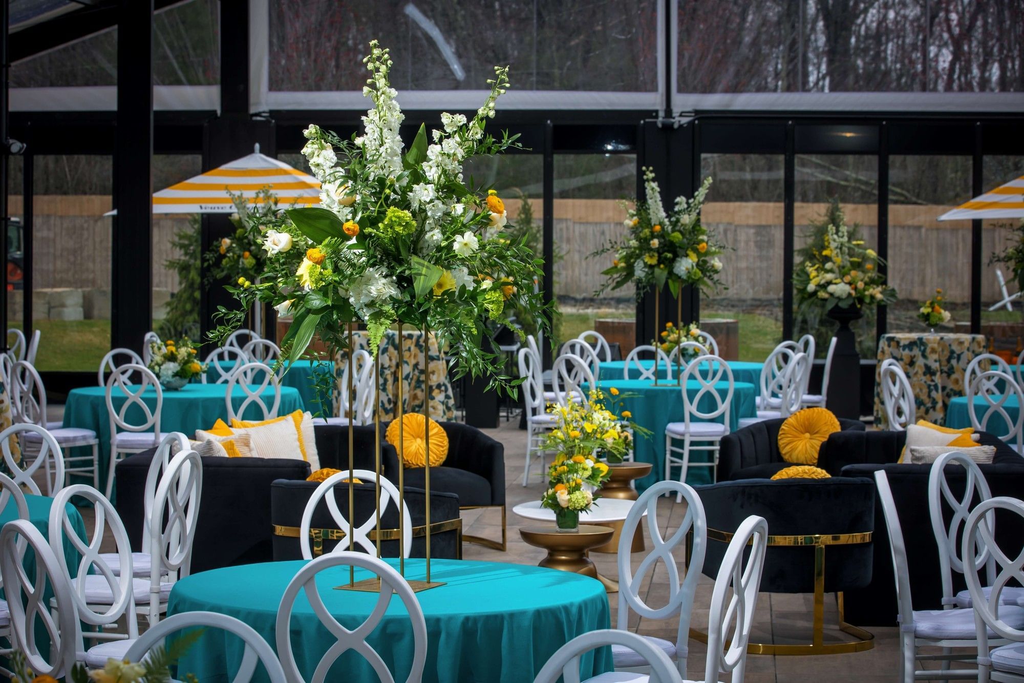 Tall floral centerpiece on teal table with white chairs and yellow accents in The Secret Garden at The Brook