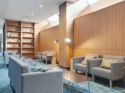 Modern communal lounge with gray sofas, wooden shelving, skylights, and blue patterned carpet at UniLodge Auckland Central