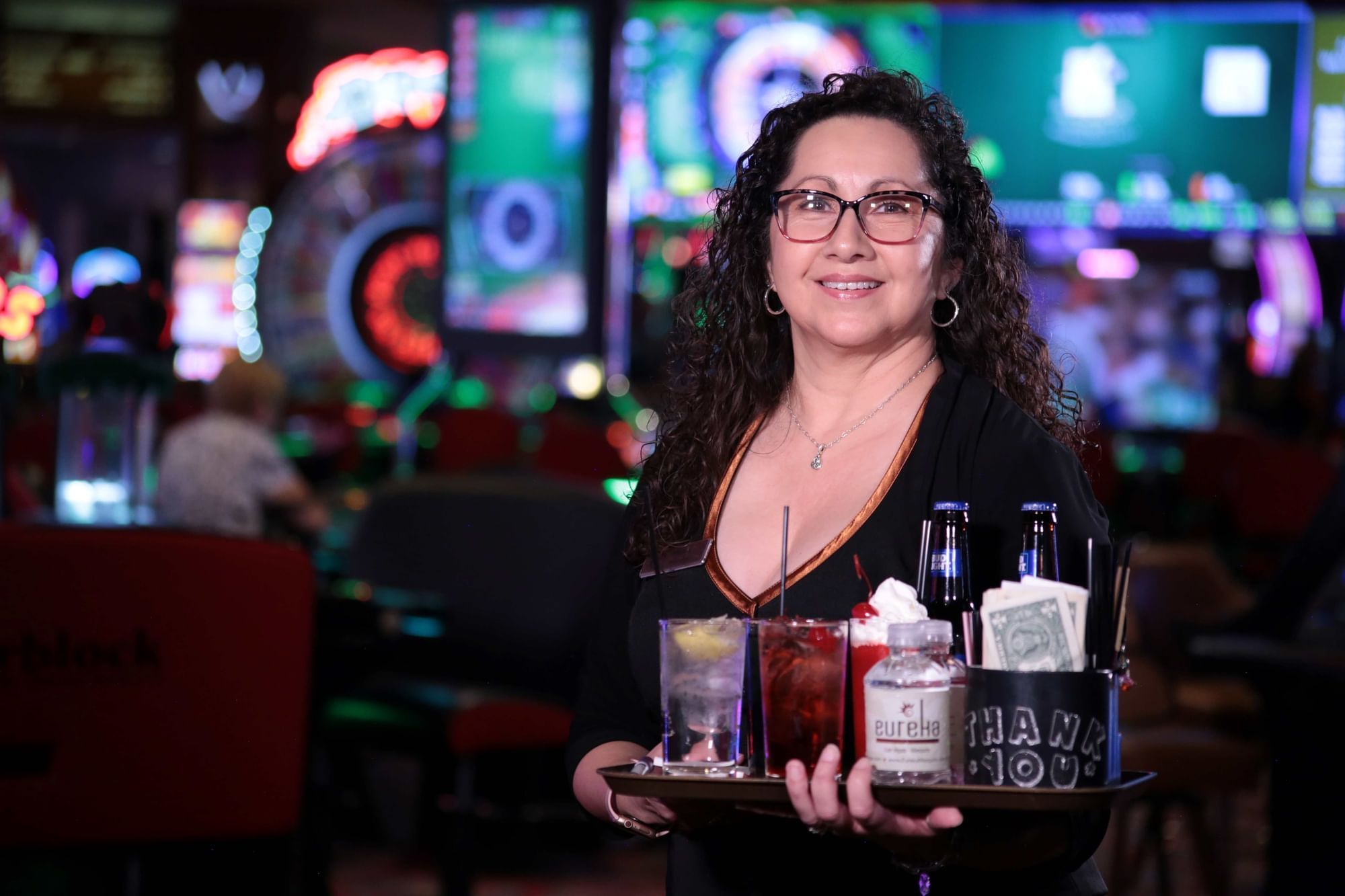 Cocktail waitress holding a drink tray filled with beverages and beer bottles near the slot floor at Eureka Casino Resort