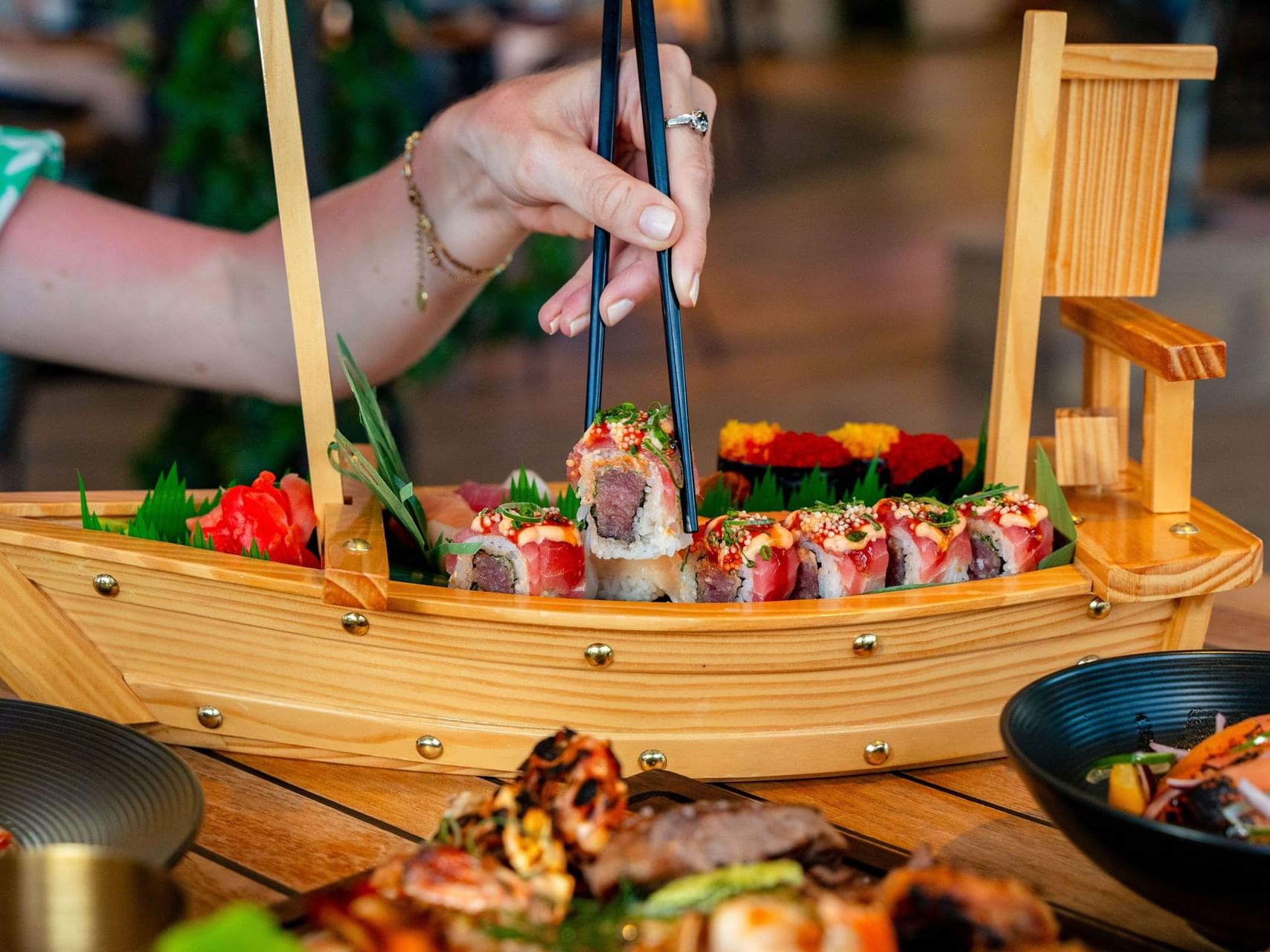 Sushi met stokjes uit een decoratieve sushiboot halen in Bobbie’s Beach Club, Golden Rock Resort