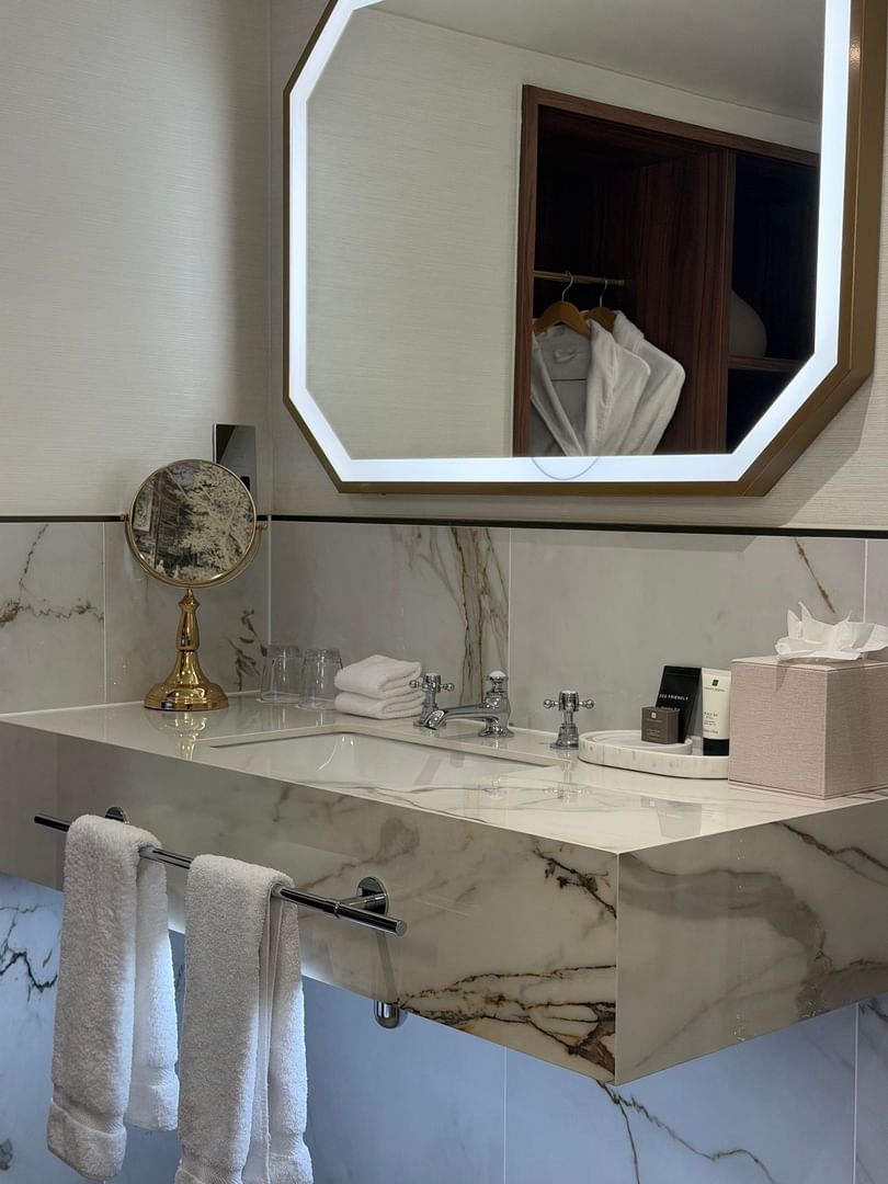 Elegant suite bathroom with marble vanity, illuminated mirror, and luxury amenities at The Capital Hotel, Apartments & Townhouse.