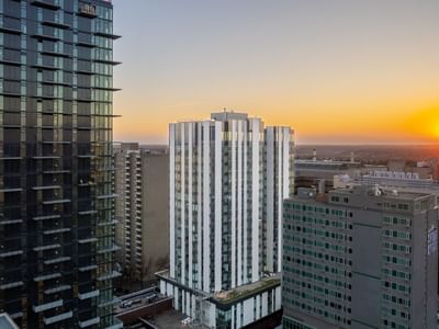 A white-coloured apartment tower surrounded by other apartment buildings, with an orange sunset in the background.