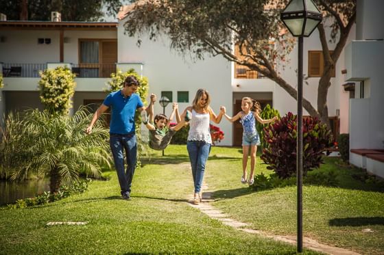 Familia de cuatro corriendo en el jardín de un complejo residencial, tomados de las manos.