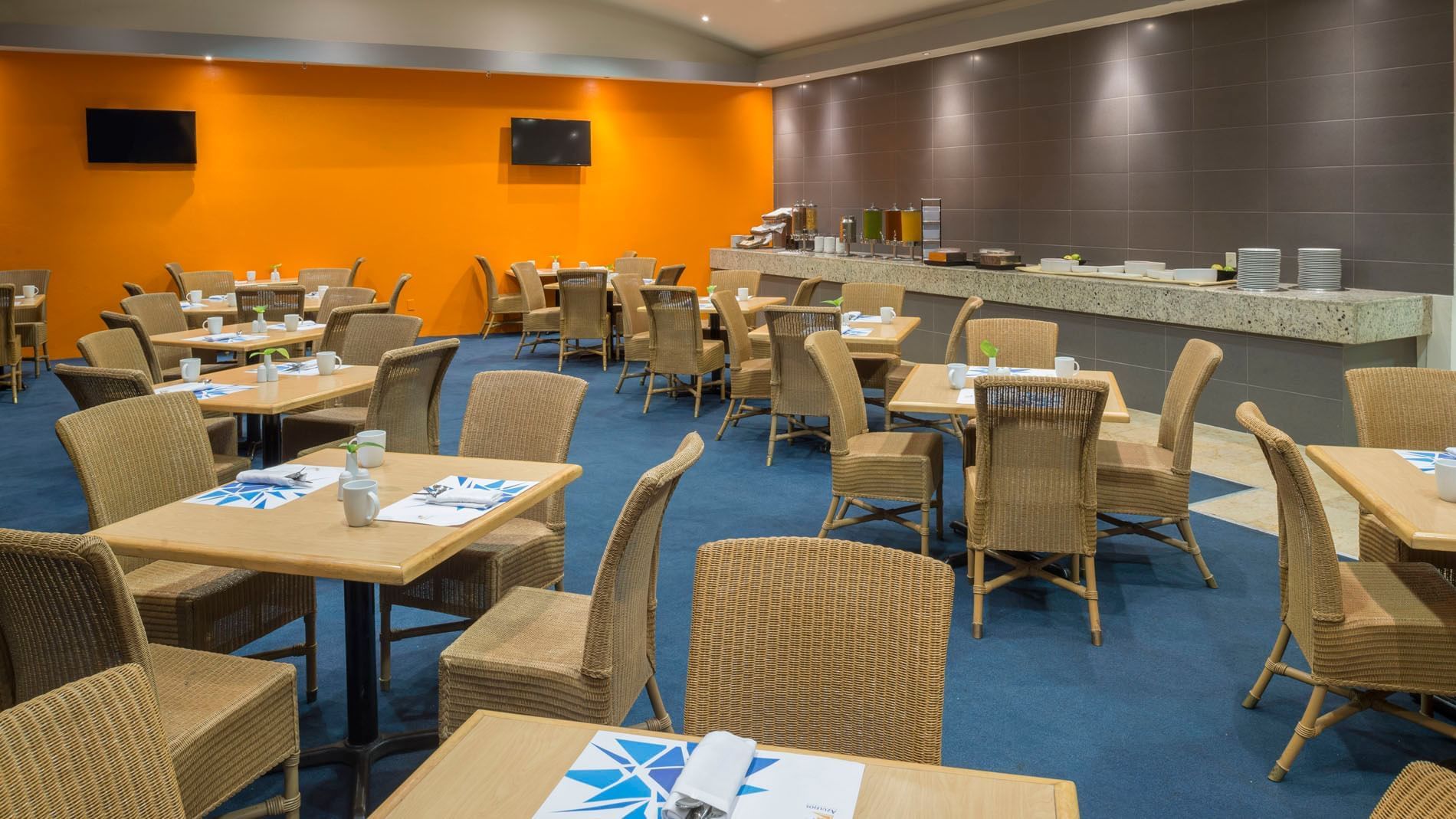 Azulejos dining area with orange walls, wicker chairs, and a buffet line at Real Inn Nuevo Laredo