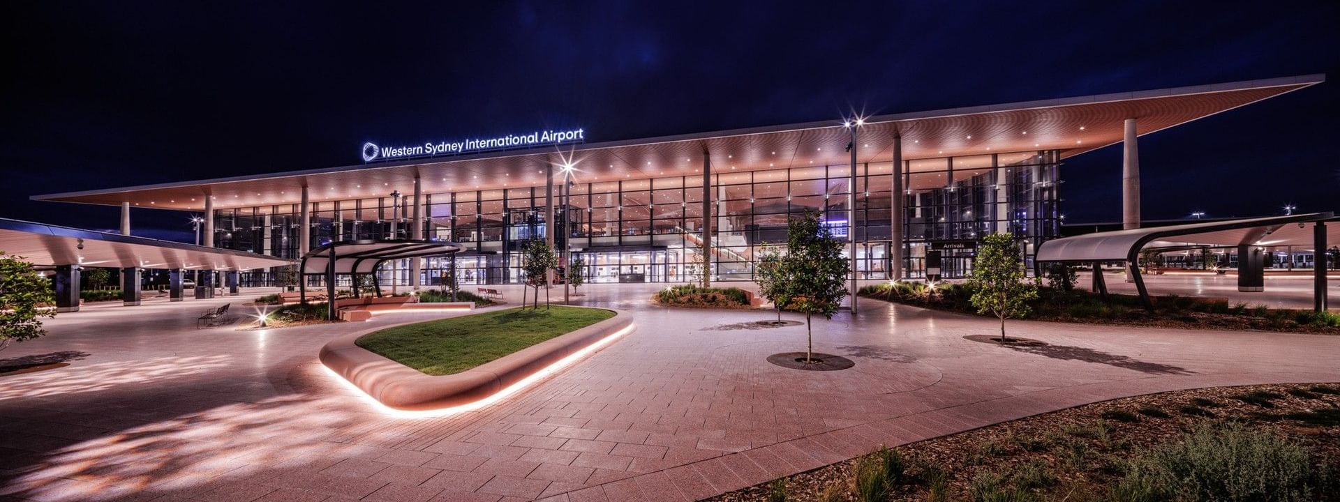 Modern illuminated terminal building with glass facade and curved roofline at Western Sydney International Airport at dusk