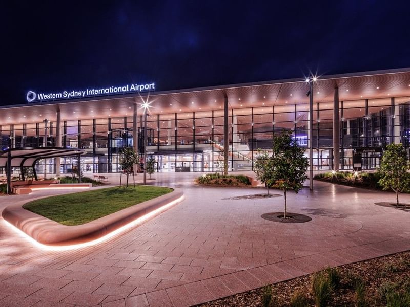 Modern illuminated terminal building with glass facade and curved roofline at Western Sydney International Airport at dusk