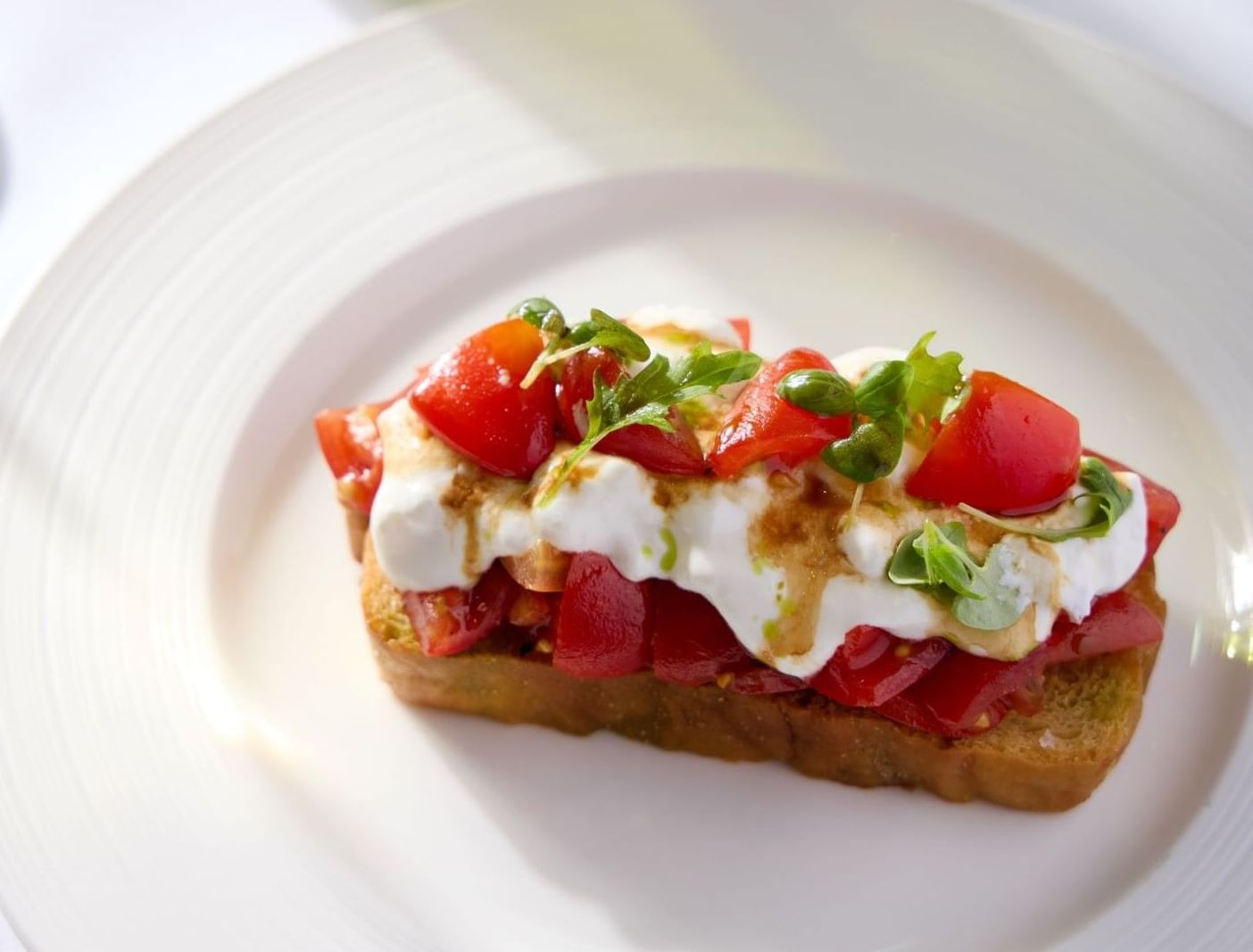 Une bruschetta ouverte garnie de tomates, de mozzarella et d'herbes aromatiques, servie sur une assiette blanche lors d'un déjeuner à l'hôtel The Londoner