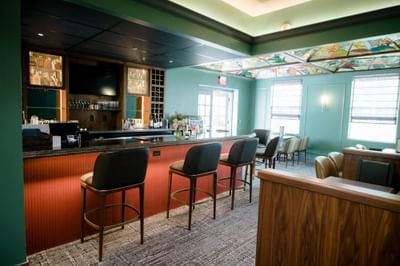 Stylish bar area with leather stools along a red counter beside stained glass ceiling detail at La Tourelle Hotel and Spa