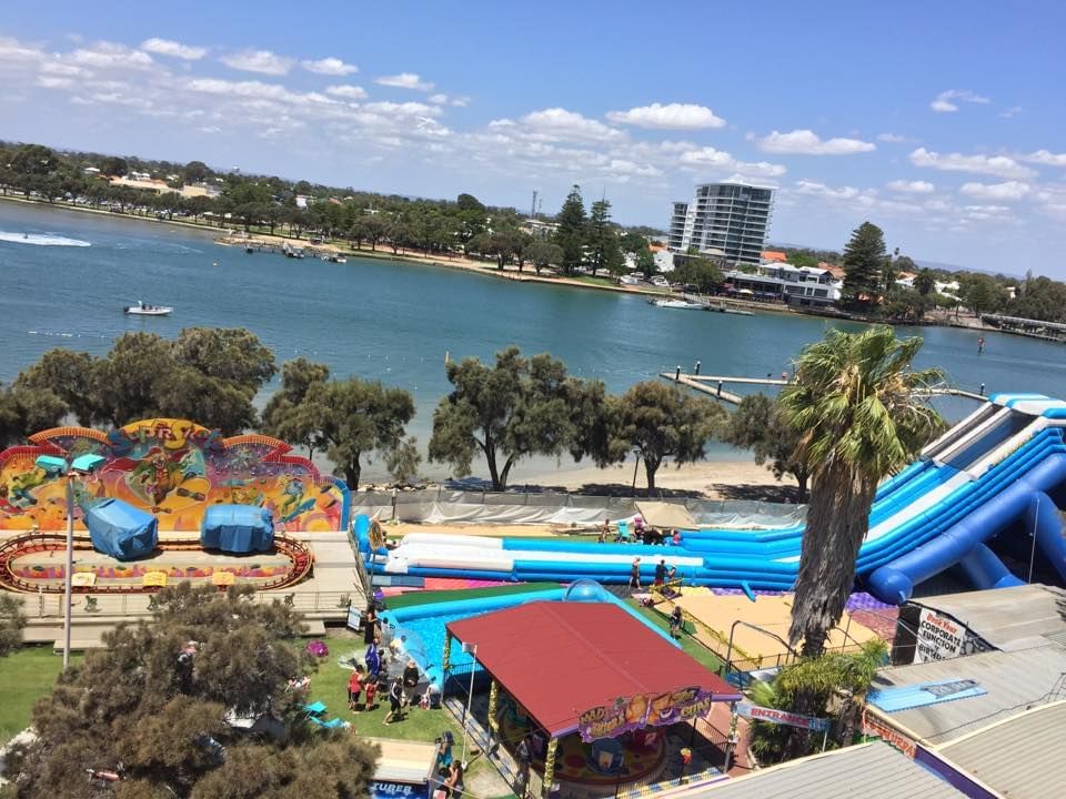 Aerial view of King Carnival amusement park by a lake, featuring rides and water slides near The Sebel Mandurah
