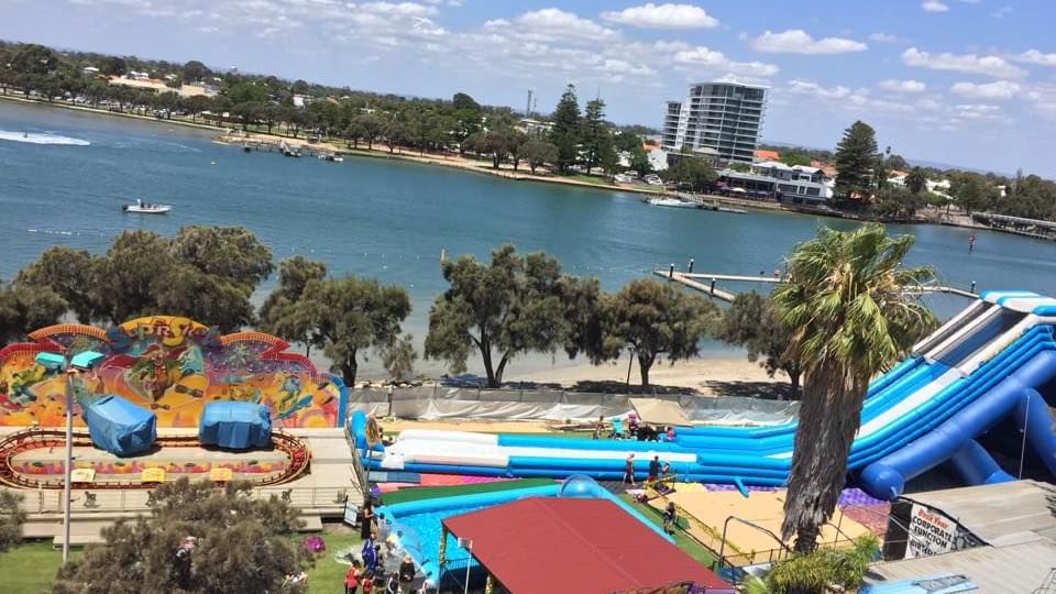Aerial view of King Carnival amusement park by a lake, featuring rides and water slides near The Sebel Mandurah