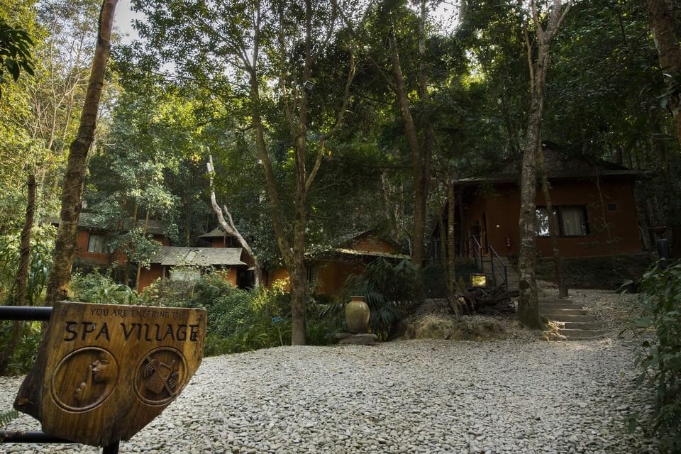 Serene Spa Village entrance with rustic cabins and stone paths nestled in lush greenery at The Dwarika's Himalayan Wellbeing